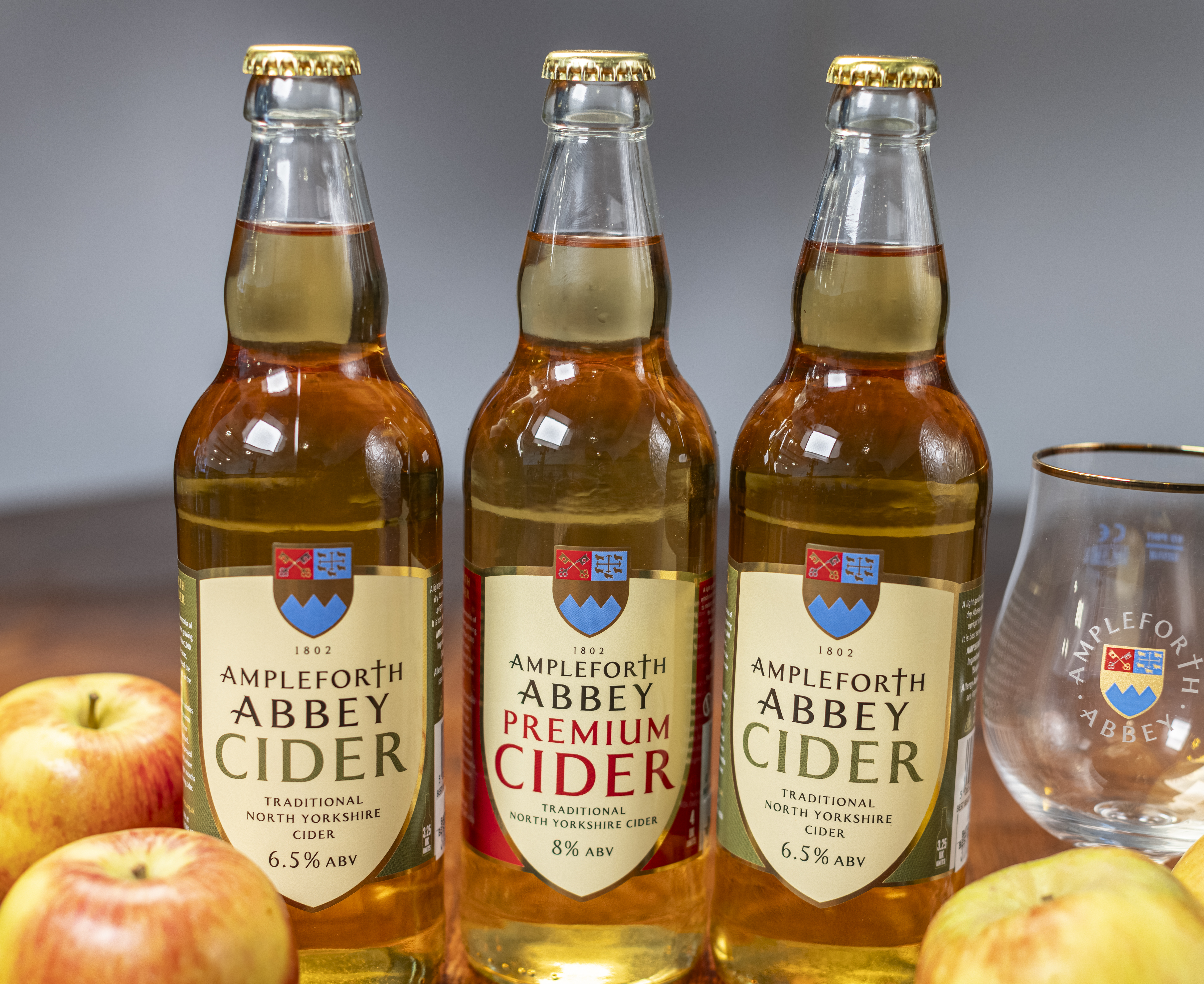 Image showing 3 glass bottles full of Ampleforth Abbey cider surrounded by apples on a wooden table.