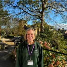 Woman with bobbed blonde hair in green Ampleforth Abbey branded uniform standing outside in front of trees and shrubs