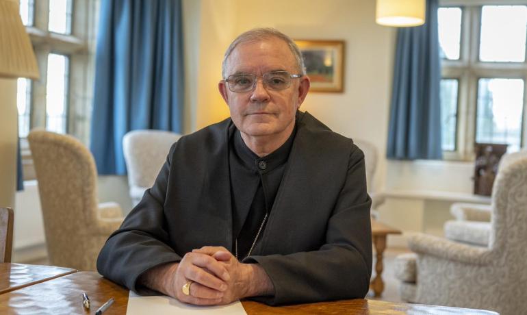 Abbot Robert with hands clasped on top of writing material at his desk