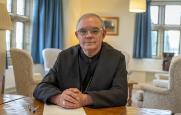 Abbot Robert with hands clasped on top of writing material at his desk